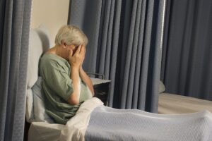 Sad elderly lady in hospital bed with hands over her face